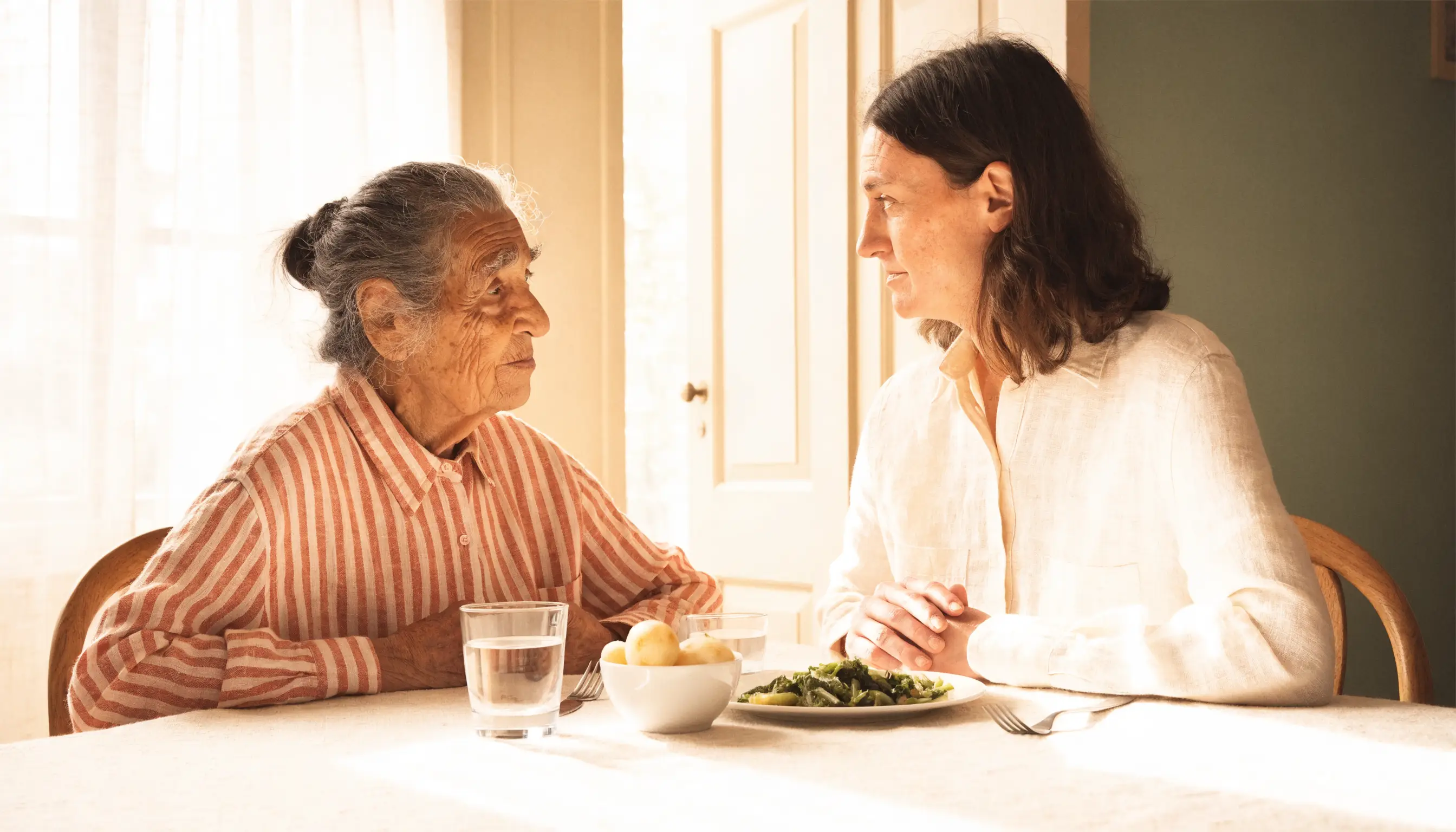 An older adult and caregiver having a calm conversation together before a meal