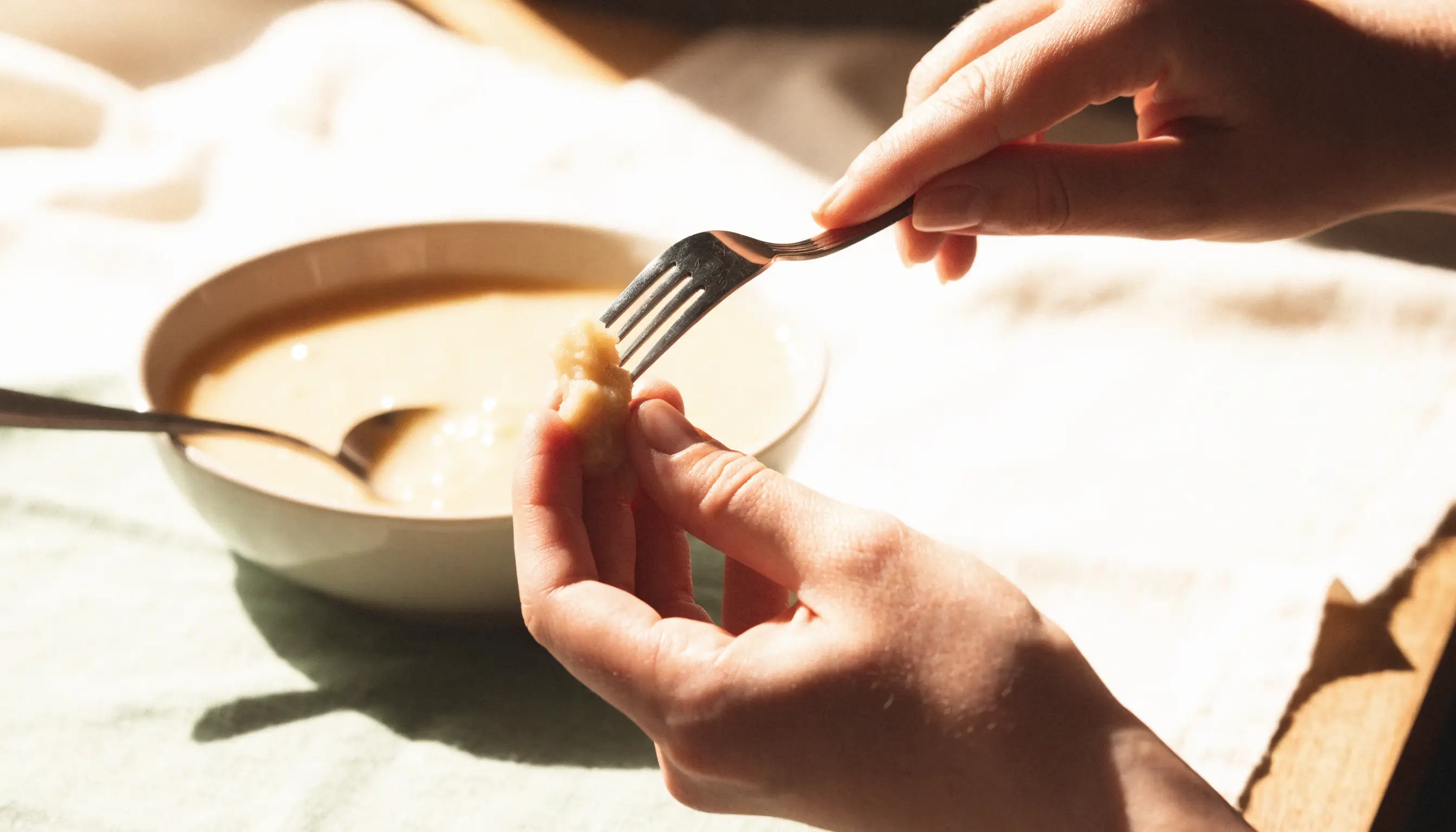 A fork gently pressing soft food beside a spoon and bowl of smooth puree